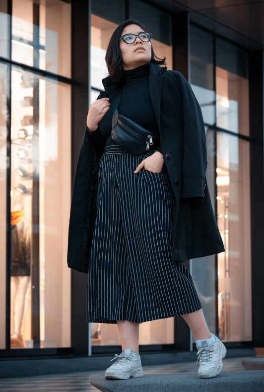 Frau mit schwarzer Culotte zu schwarzem Mantel und Chunky Sneakern