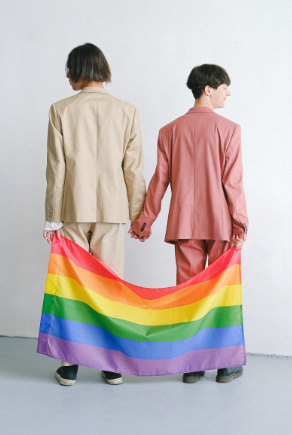 Zwei Personen Hand in Hand von hinten mit Regenbogenflagge