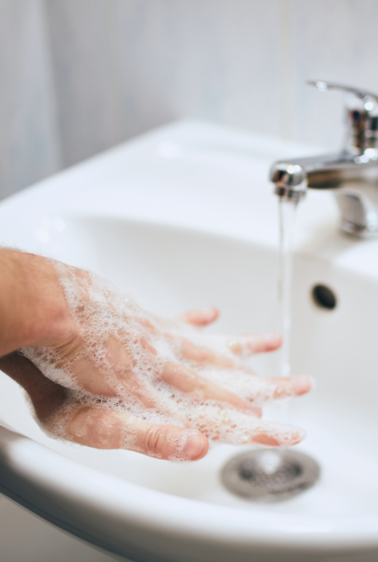 Person, die sich unter fließendem Wasserhahn mit Seife die Hände wäscht