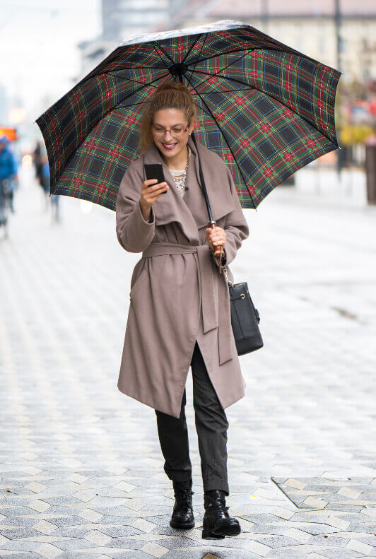 Street Style: Frau mit rosa Trenchcoat und kariertem Regenschirm