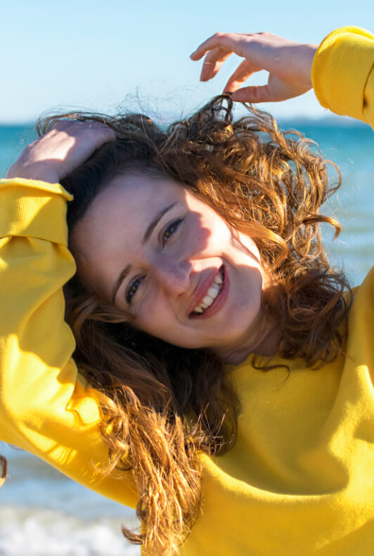 Frau am Strand mit lockigen Haaren und Pullover in Gelb
