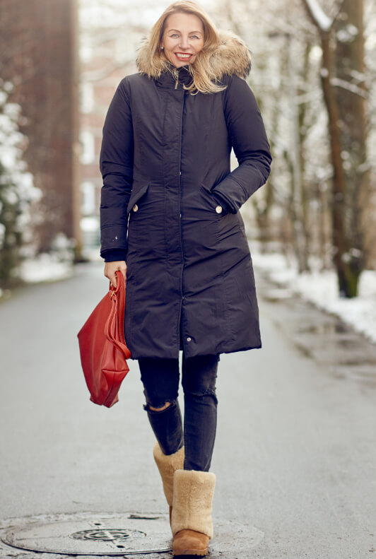 Frau im Winter-Parka mit Destroyed-Jeans und Ugg Boots in Beige