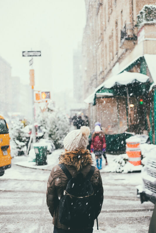 Frau im Winter mit einer weißen Mütze vor einer verschneiten Straße
