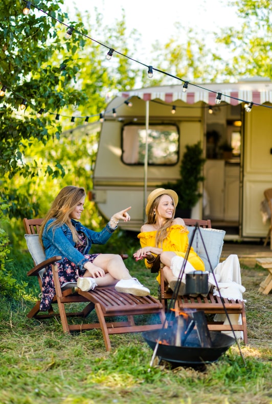 Twee jonge vrouwen liggen op een kampeerplek voor een caravan