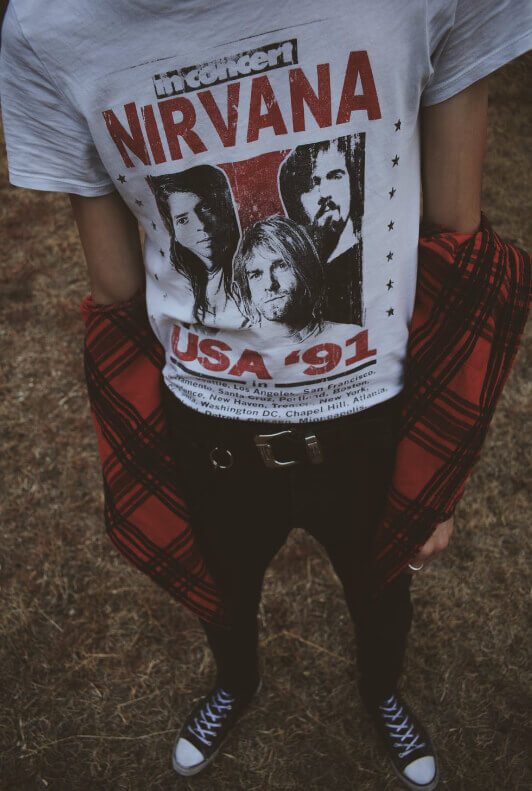 Mann trägt Nirvana-Shirt, rot-schwarz kariertes Hemd, Chucks und schwarze Jeans