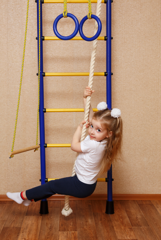 Kleines Mädchen spielt an einem Seil während sich im Hintergrund Ringe und eine Sprossenwand befinden