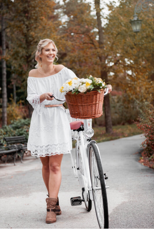 Frau mit Fahrrad trägt weißes Kleid und Ankle Boots