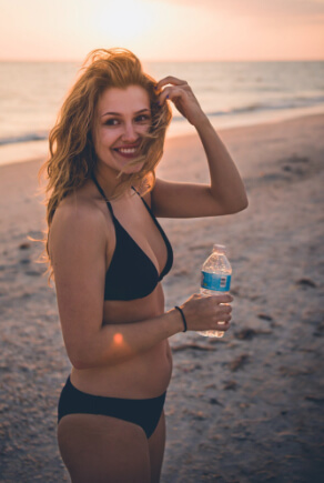 Lächelnde Frau mit Beach Waves im schwarzen Bikini am Strand